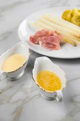 Weißer Spargel mit Sauce Hollandaise, zerlassener Butter, geräucherter Schinken und Kartoffeln auf Teller und Marmor Hintergrund