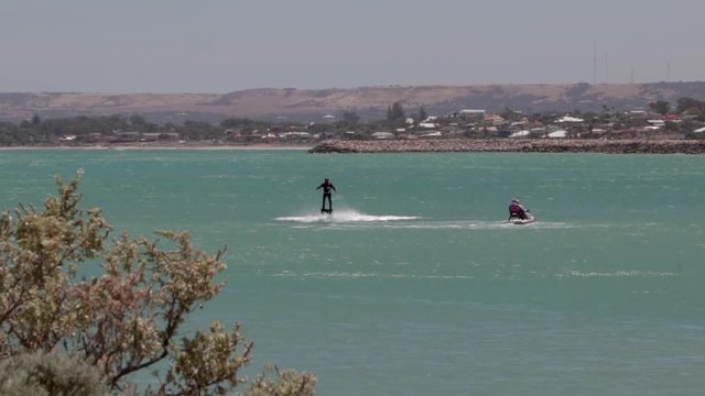 shot over the ocean of a person riding a flyboard behind a jet ski.