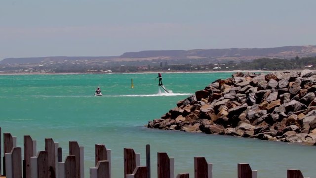 shot over the ocean of a person riding a flyboard behind a jet ski.