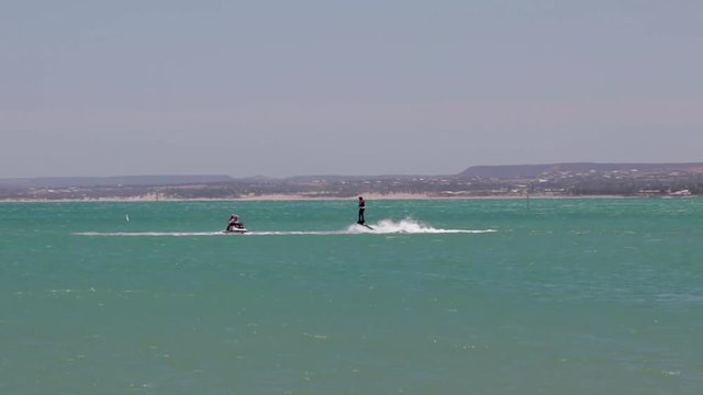 shot over the ocean of a person riding a flyboard behind a jet ski.