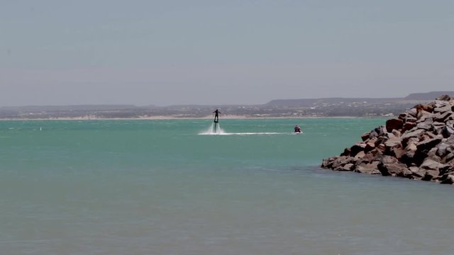 shot over the ocean of a person riding a flyboard behind a jet ski.