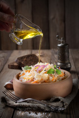Sauerkraut with onions and mint, in a pottery,pour olive oil. Pieces of black rye bread and a pepper shaker on the back of a wooden background.