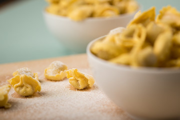 Frische, rohe Cappelletti Tortellini Pasta mit Mehl und Grieß in Porzellan Schale auf Holz Brett und Pastell Grün Hintergrund