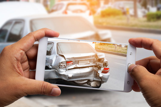 Car insurance agents take pictures of accident-damaged vehicles with  smartphone for proof of insurance claim.