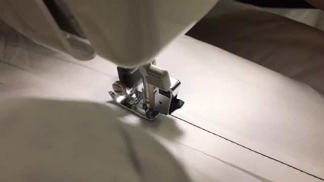 Worker stitches cloth on the sewing machine. Cratches the thread on the fabric.