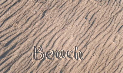 Fototapeta na wymiar The word beach is written on the sand by hand. Beach season. Postcard. Shadows on the sand.