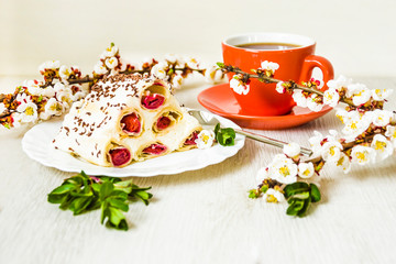 Dessert cake cherry slide, a cup of black tea and flowering branches of apricot. On wooden background