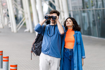 Young pretty couple - a boy and a girl walking around the city with a binocular in his hands. Young people travel.