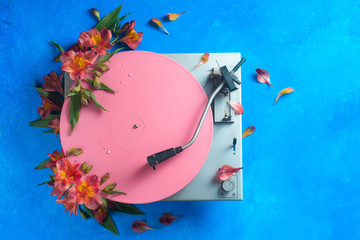 Pink color block flat lay with colorful vinyl record player and flowers. Spring music still life...