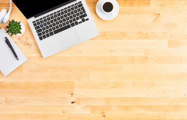 Modern laptop computer. Top view of wooden office desk with laptop computer, headphone, pen, notebook, plant and cup of coffee. Modern office. Copy space for text.
