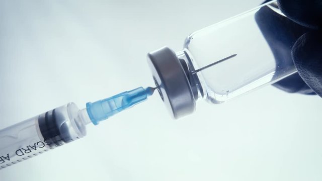 Closeup of a doctor filling a syringe with vaccines. Needle of the immunization device punctures the rubber seal of the glass vial, drawing in the medicine.