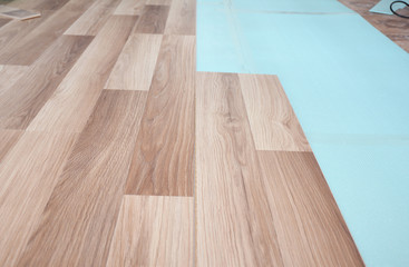 Installing wooden laminate flooring with insulation and soundproofing sheets.