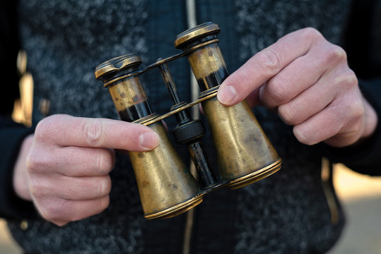 Man Is Holding In Hands A Brass Vintage Binoculars Close Up.