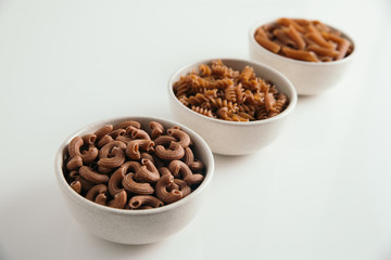 Variety of whole grain pasta, white background, selective focus (elbow macaroni in focus), diagonal
