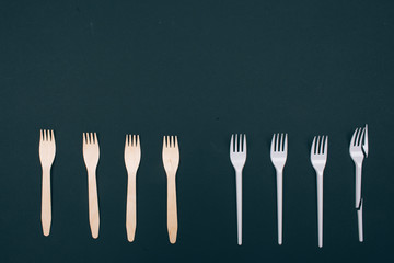 Be plastic free. Zero waste. Eco-friendly natural and single-use forks in the row on dark background, top view. Reduce reuse recycle. Single-use plastic or reusable recyclable product