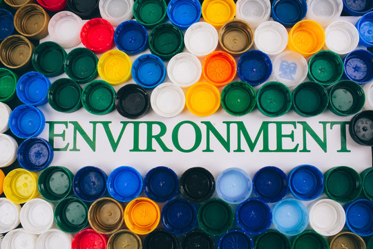 Plastic pollution concept. Be plastic free. Word Environment in the center of colored background of different plastic lids, top view. Single-use plastics, EU European directive to help environment - Powered by Adobe