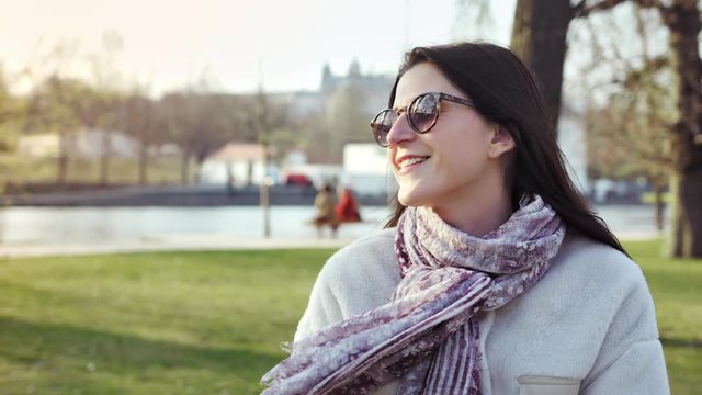 Medium close-up smiling stylish woman enjoying walking in autumn city park or garden at sunset