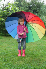 Little girl standing under umbrella in a rain outdoors