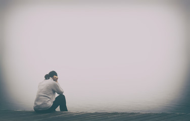 Junge Frau sitzt einsam am Rand eines Holzweges einer Brücke gebückt und traurig in Gedanken. Copy Space.