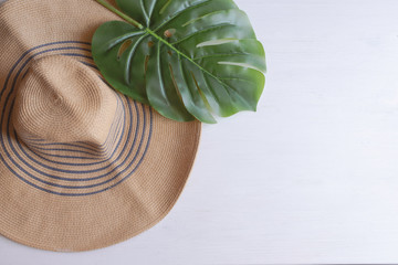 Big straw hat with palm leaf on white wooden background. Summer vacation background with copy space.