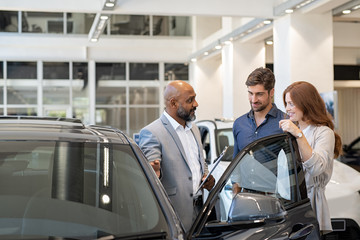 Couple examining new auto with car dealer