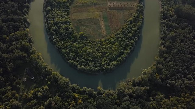 Birds eye view over the Prut river meander; mimimalistic, geometrical shot with river arch surrounded by lush warm green forests and farming land in the inner circle