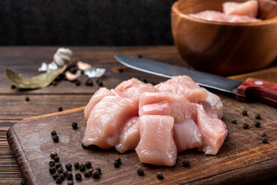 Diced raw chicken breast or fillets on dark wooden background.