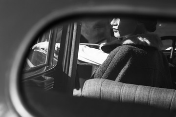 Woman dressed in old-fashioned style sits in a retro car together with her man