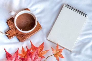 Flay lay of of a cup of coffee with blank notebook with red maple in Autumn. Copy space and background.