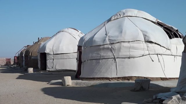 A wide, still shot of several covered yurts in a row in a town in Uzbekistan on a windy day