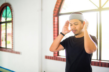 Young muslim man praying hands up for takbir inside a mosque