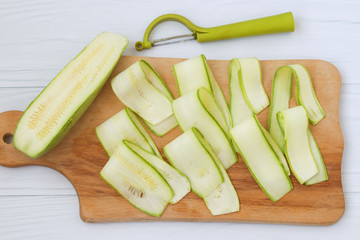 Zucchini, cut with ribbons using vegetable cutters. Located on a wooden board on a white background, top view