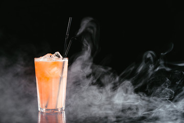 Orange cocktail with fruit on a black smoky background.