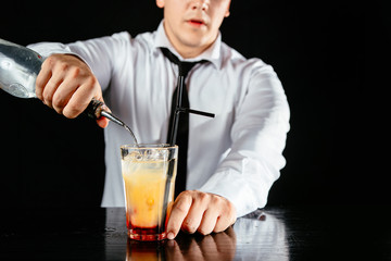 Barman makes a two colored cocktail on a black counter, black background. 