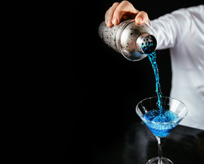 Barman making a blue martini cocktail on a black counter and background.