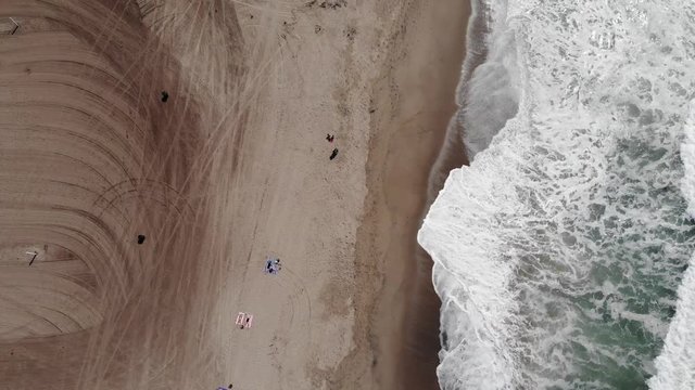 Birdseye view drone footage of a beautiful beach with waves crashing against the soft white sand. Shot at Zuma Beach in Malibu, California.