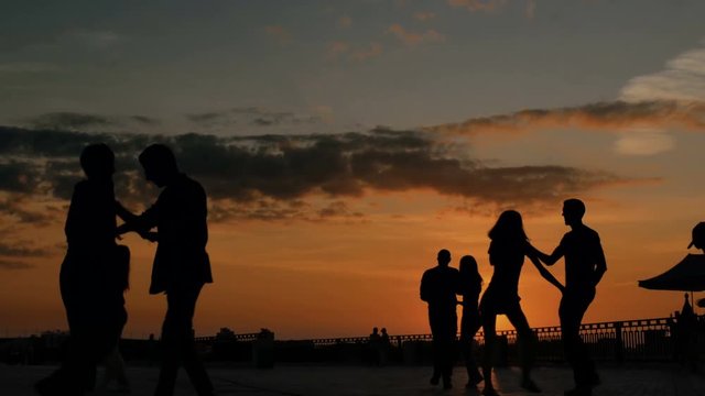 Unrecognizable people silhouette learning how to dance on city quay at sunset. Street dance, romantic and urban culture concept