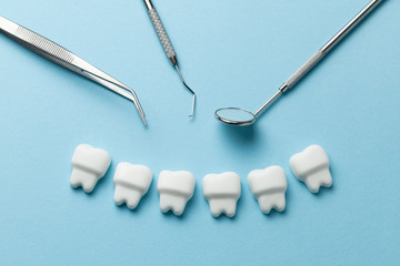 Healthy white teeth on blue background and dentist tools mirror, hook.