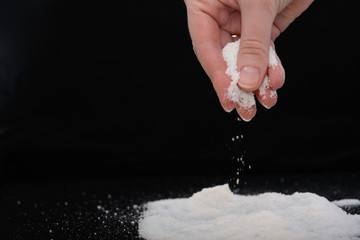 in the fingers of a young woman a pinch of salt, which she pours down on a hill of salt. Image on black background. Concept - salt-free diet.