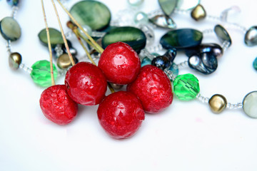 Frozen cherry and necklace with precious stones on a white plate. Image on black background. Concept - table decoration