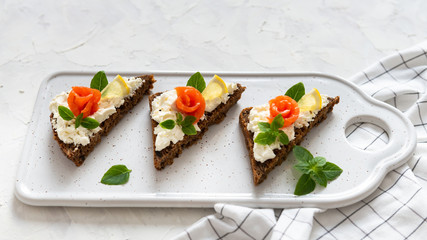 Sandwich with cereals bread, salmon, fresh cheese, basil and lemon on white background. Top view