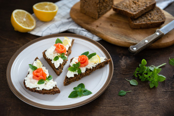 smoked salmon sandwich with fresh cream, lemon and basil on white plate. Healthy breakfast concept. Wholegrain bread, copy space