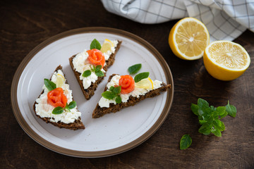 smoked salmon sandwich with fresh cream, lemon and basil on white plate. Healthy breakfast concept. Wholegrain bread