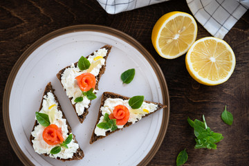 Sandwich with cereals bread, salmon, fresh cheese, basil and lemon on white background. Top view, copy space