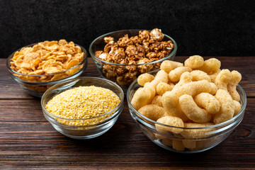 Corn sticks, corn flakes and popcorn on dark wooden background.