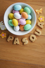 Easter background with colorful chocolate eggs in a bowl  with cookies in shape of "Pasqua" on wooden background