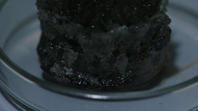 Light grey naturally occurring mineral standing in a glass laboratory utensils on the table. Stock footage. Chemistry experiments