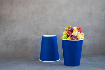 Two blue paper cups with multi-colored caramel popcorn on gray background.