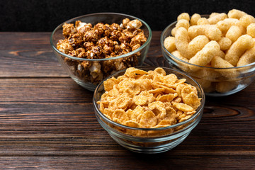 Corn sticks, corn flakes and popcorn on dark wooden background.