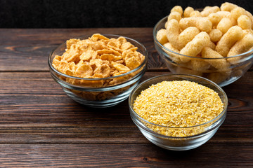 Corn sticks, corn and corn flakes on dark wooden background.